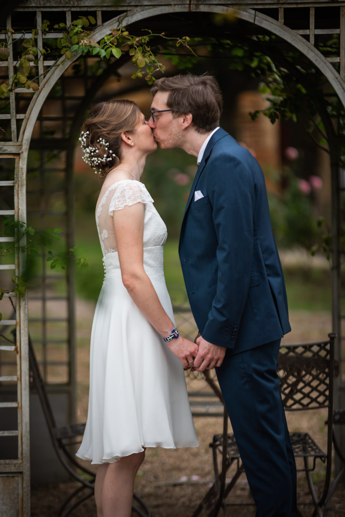 Laure et Mathieu s’embrassant sous une arche de jardin au Domaine de la Ruisselière, à Lacenas