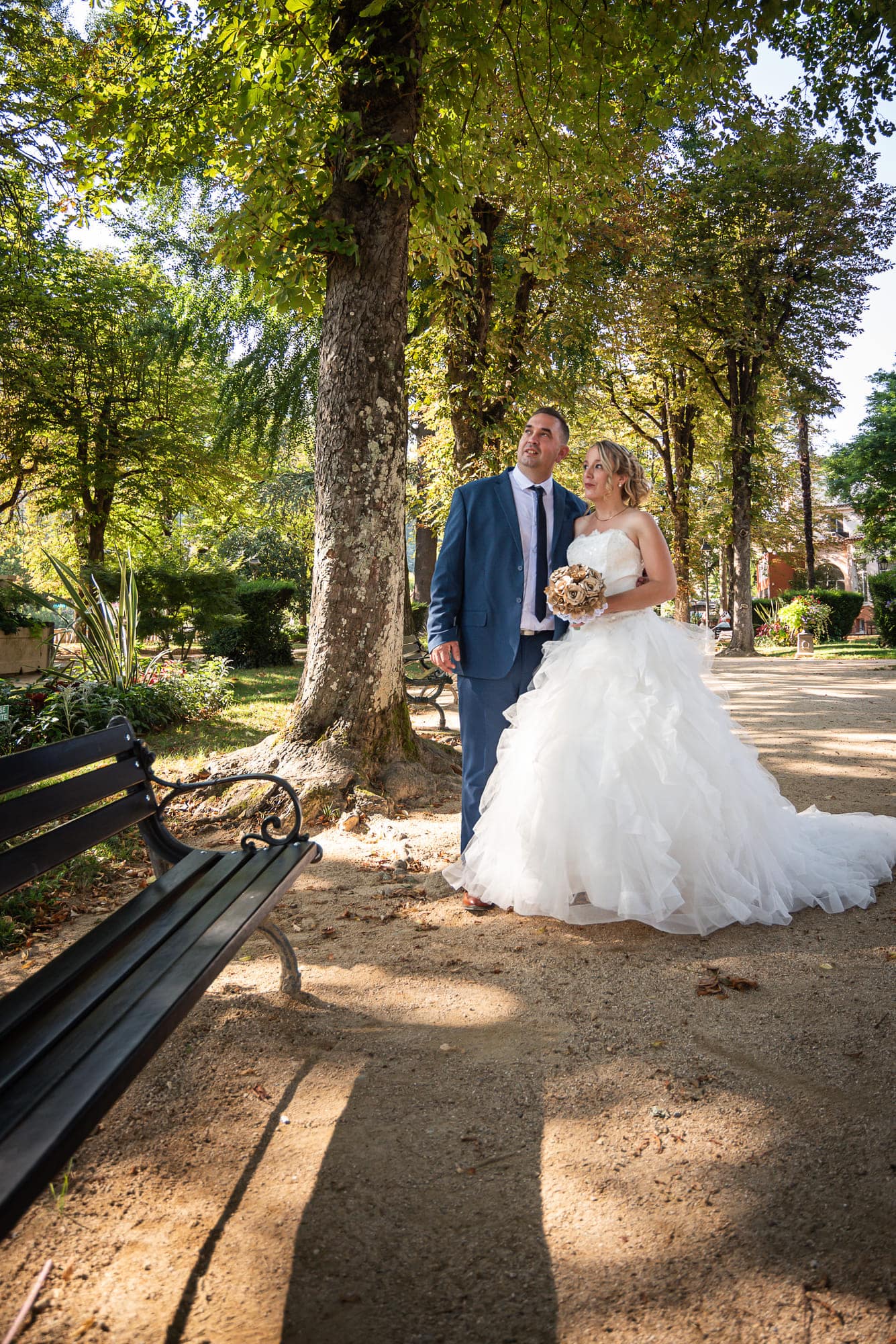 Mariés dans une allée de parc, regardant vers la canopée des arbres