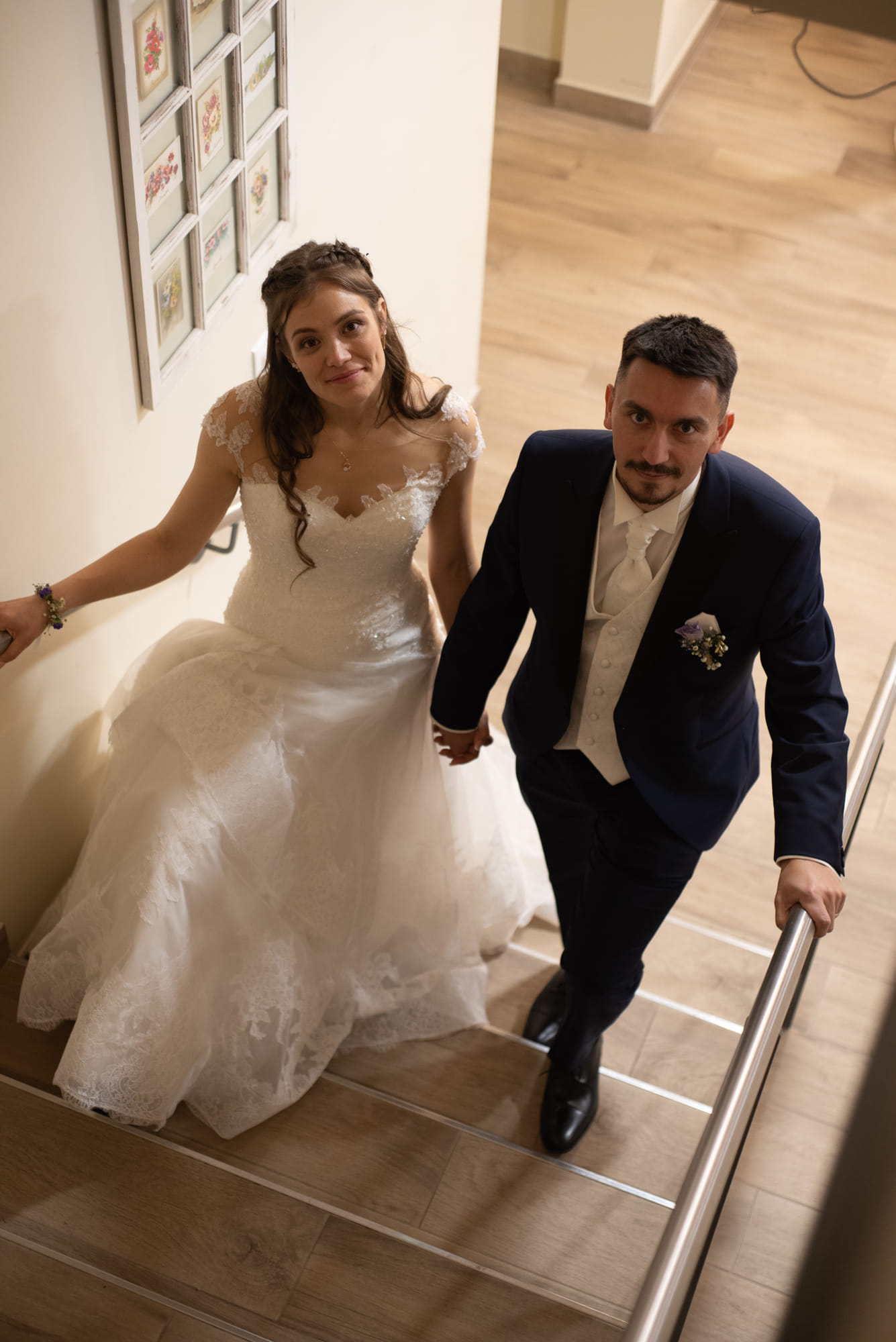 Mariés montant un escalier en se tenant la main, regard vers l’objectif
