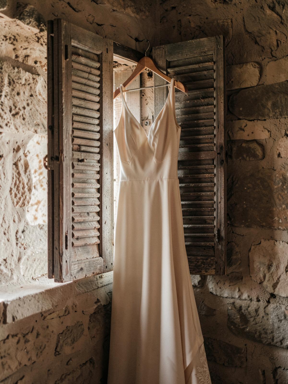 Robe de mariée suspendue devant des volets anciens en pierre