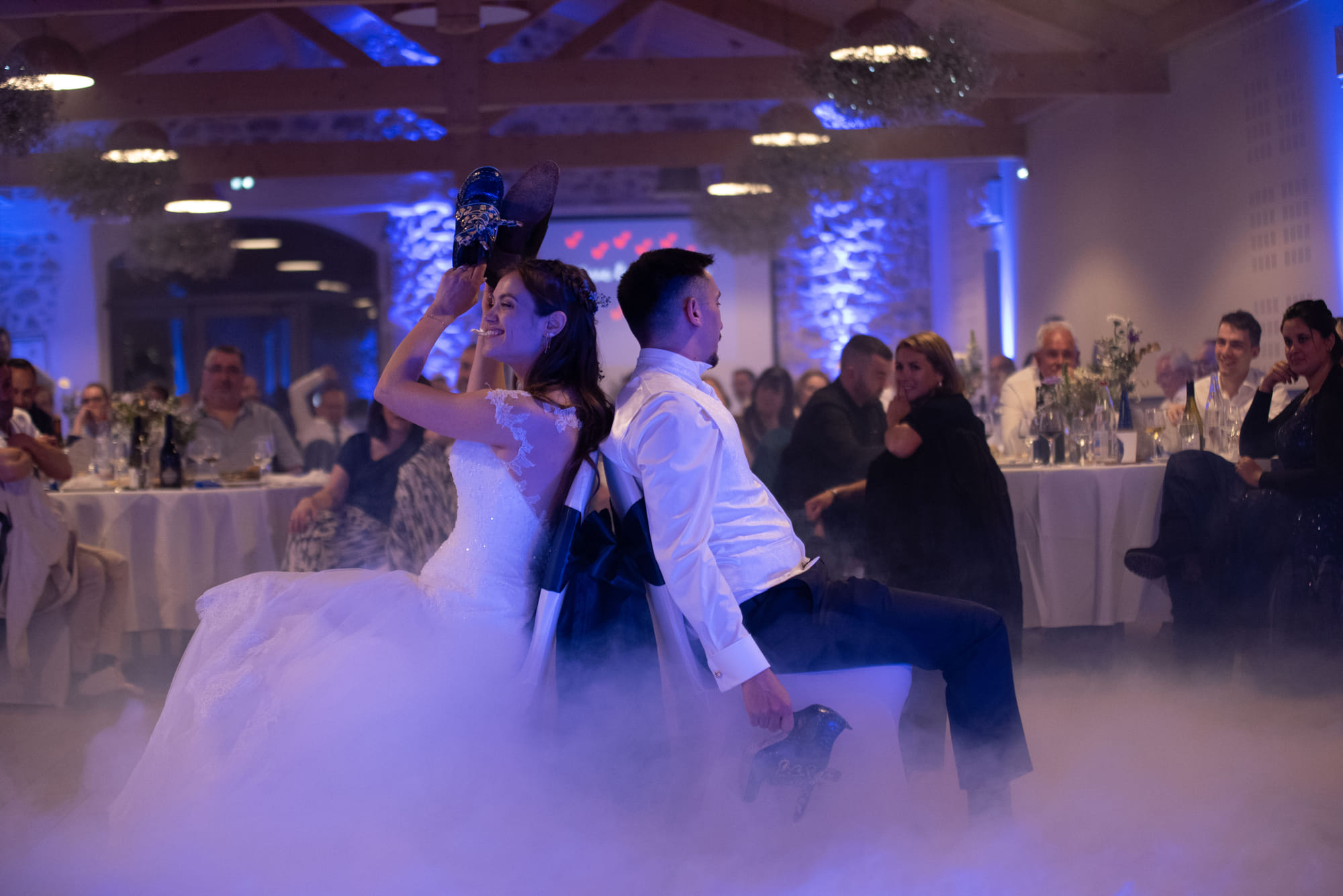 Mariés dos à dos pendant le jeu des chaussures, dans la brume de la piste de danse