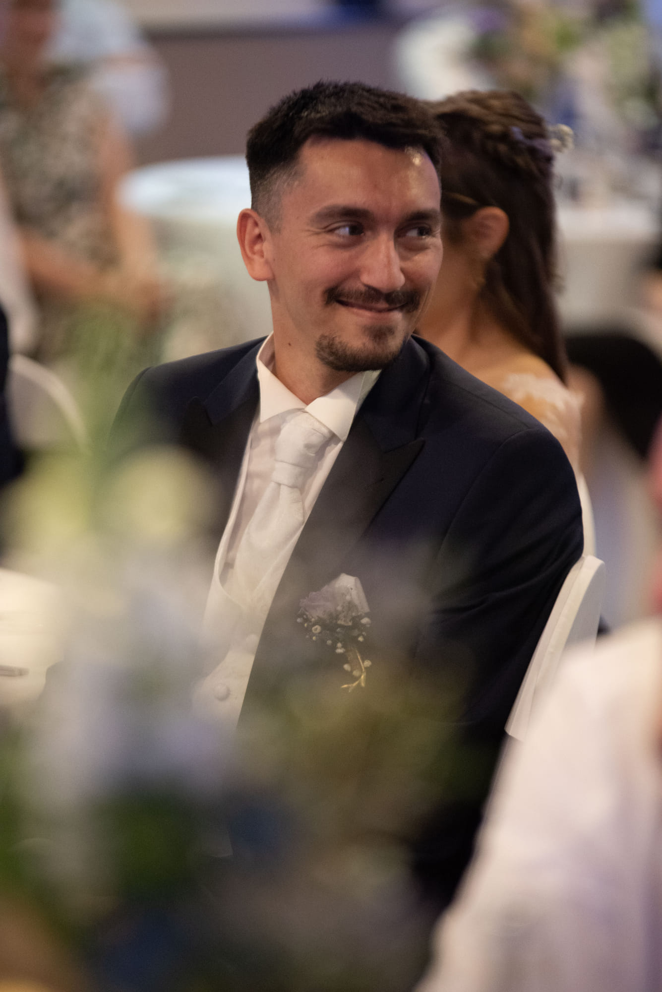 Portrait d’un invité souriant pendant la réception, fleurs au premier plan