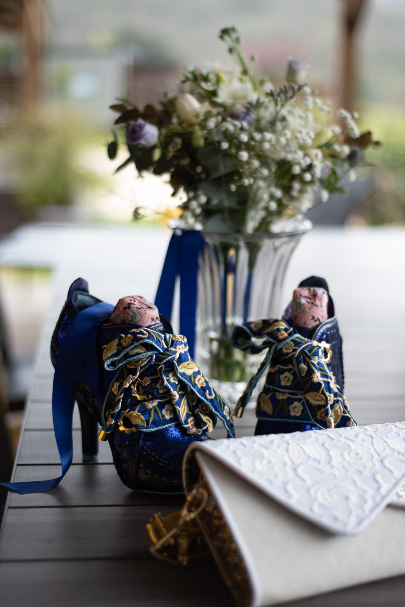Souliers de mariée bleu roi brodés, posés à côté d’un bouquet